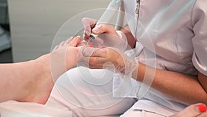 Pedicurist woman removes red shellac polish from toes using manicure machine.