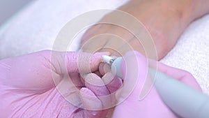 Pedicurist woman removes shellac polish from toes using manicure machine.