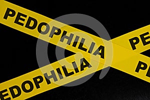 Pedophilia caution and warning concept. Yellow barricade tape with word in dark black background.