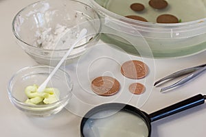 Peeled copper coins lie on the table surface. Corroded coins are lying nearby in a container with phosphoric acid. Sulfuric