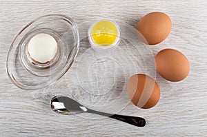 Peeled egg on egg stand, spoon, salt shaker, boiled eggs on wooden table. Top view