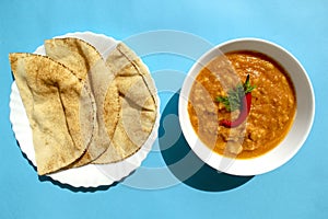 Peeled fava beans with chilli in a white bowl and pita bread on blue background. Top view. Foul Mudammas, Egyptian beans, flatbrea