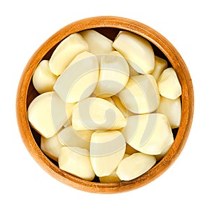 Peeled garlic cloves in wooden bowl over white