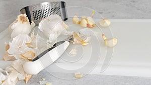 Peeled garlic, garlic press, and kitchen knife close-up on a white plastic cutting board