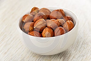 Peeled hazelnuts in white bowl on wooden table