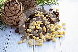 Peeled kernels of cedar nuts in a spoon, two pine cones, green branches