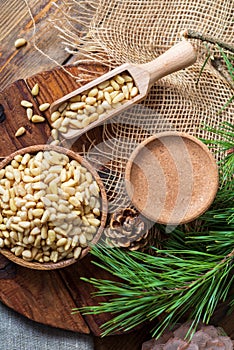 Peeled pine nuts in a bowl, pine cone on a cutting board, rough cloth next to it. View from above. Healthy food of