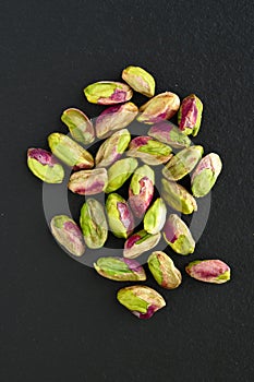 Peeled pistachios on the black stone board, top view