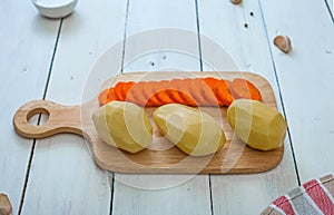 Peeled potatoes and carrots in a sliced on a cutting board