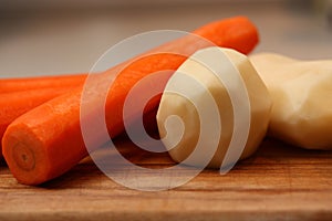 Peeled potatoes and carrots on wooden chopping board.