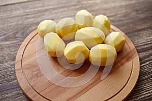 Peeled potatoes on wooden cutting board on brown table. Cooking food from natural products. Root vegetable ingredient: