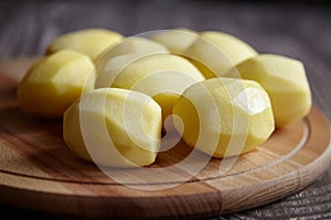 Peeled potatoes on wooden cutting board on brown table. Cooking food from natural products. Root vegetable ingredient: