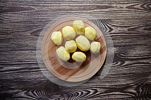 Peeled potatoes on wooden cutting board on brown table. Cooking food from natural products. Root vegetable ingredient: