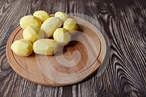 Peeled potatoes on wooden cutting board on brown table. Cooking food from natural products. Root vegetable. Raw ingredient