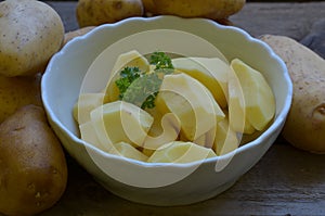 Peeled potatoes with parsley in white bowl on wooden background