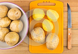 Peeled raw potatoes on cutting board, glass bowl