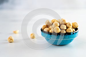 Peeled roasted hazelnuts in a blue round ceramic bowl stands on a white plate. Healthy and wholesome food high in protein.
