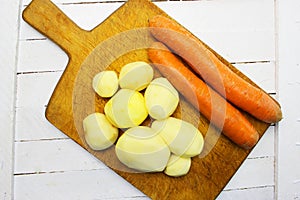 Peeled round potatoes a huge pile of very large fresh and sweet carrots on a white wooden table. beautiful fresh market