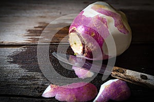 Peeled rutabaga with knife lying on rustic wood background