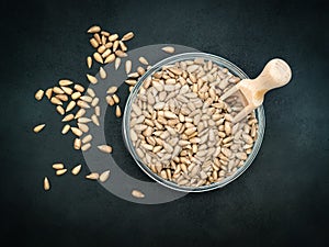 Peeled sunflower seeds in a glass bowl with a small wooden spoon on the black background. Close-up