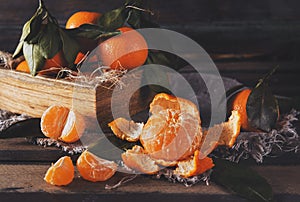 Peeled tangerine, whole tangerines with leaves in a box  on a brown wooden