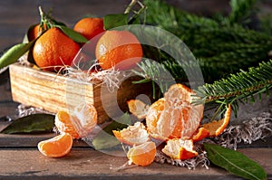 Peeled tangerine, whole tangerines with leaves in a box , fir branches on a brown wooden
