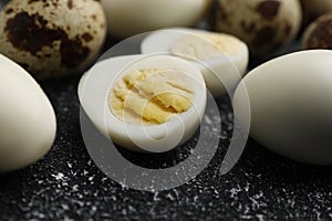 Peeled and unpeeled hard boiled quail eggs on black table, closeup