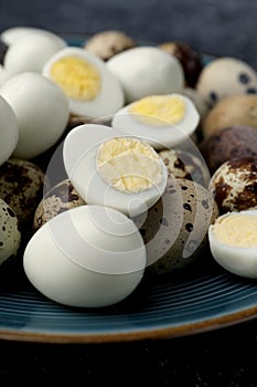 Peeled and unpeeled hard boiled quail eggs in plate on black table, closeup