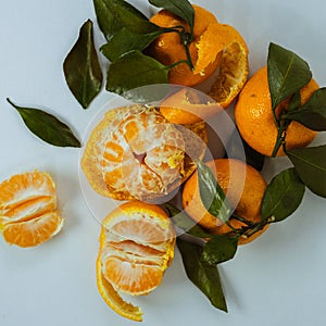 peeled and unpeeled tangerines lie on a white table. Fresh mandarin oranges fruit or tangerines with leaves on a table