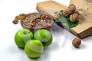 Peeled walnuts in wooden bowl, green apples, firewood