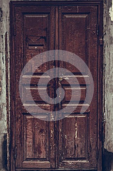 Peeling brown wooden door. Dilapidated wooden grunge door with cracked maroon paint. Threadbare dark red door.