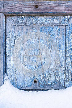 Peeling paint on the old door in the snow. A pattern of rustic blue grunge material. Abstract background.