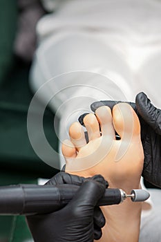 Peeling pedicure procedure on the sole from callus of the female foot by a pedicurist at a beauty salon.