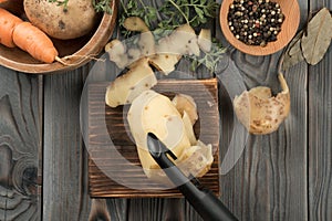 Peeling yellow potato with vegetable peeler. Flat lay view. Fresh raw potato. Cutting peel on kitchen wooden board.