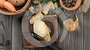 Peeling young yellow potatoes with vegetable peeler. Stop motion, flat lay. Cutting peel on kitchen wooden board.