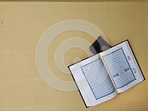 Peka Islamic background for Eid al Fitr. An open page of Quran shows Surah Al Kahf. A madinah manuscript on light brown background