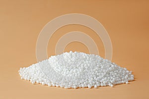 Pellets of ammonium nitrate on beige background, space for text. Mineral fertilizer