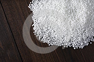 Pellets of ammonium nitrate on wooden table, flat lay with space for text. Mineral fertilizer