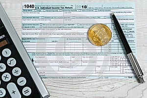 The pen, bitcoins and calculator on the tax form 1040 U.S. Individual Income Tax Return. The time to pay taxes