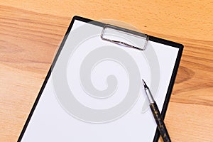 Pen on blank white document sheet on wood clipboard on white wood table top view space