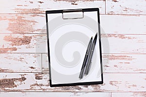 Pen on blank white document sheet on wood clipboard on white wood table top view space