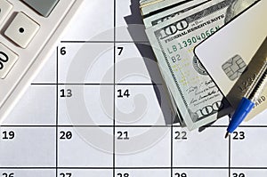 Pen and credit card on many hundred US dollar bills and calculator on calendar page close up