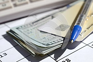 Pen and credit card on many hundred US dollar bills and calculator on calendar page close up