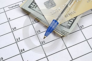 Pen and credit card on many hundred US dollar bills on calendar page close up