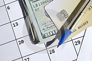 Pen and credit card on many hundred US dollar bills on calendar page close up