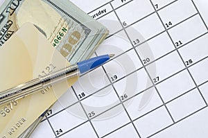 Pen and credit card on many hundred US dollar bills on calendar page close up