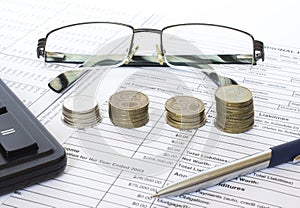 Pen on financial and accounting reports with coins stacks, glasses and calculator