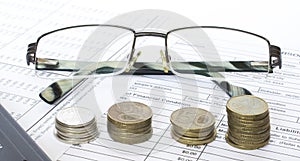 Pen on financial and accounting reports with coins stacks, glasses and calculator