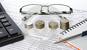 Pen on financial and accounting reports with coins stacks, glasses and calculator in background.