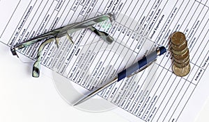 Pen on financial and accounting reports with coins stacks, glasses and calculator in background